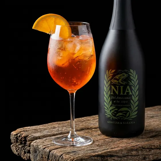 Copa con spritz naranja y una rodaja de naranja, junto a la botella de Nía Guayusa & Naranja