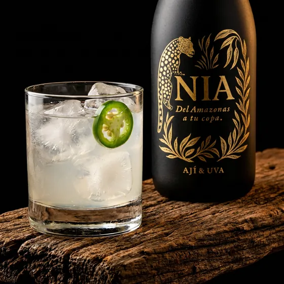 Vaso con hielo y una rodaja de jalapeño junto a la botella de Nía sobre madera oscura