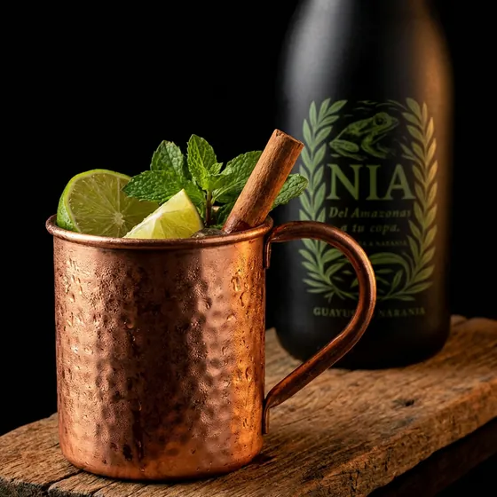 Mug de cobre con lima, hierbabuena y canela, junto a la botella de Nía Guayusa & Naranja