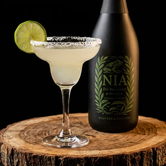 Copa de margarita con borde de sal y lima, junto a la botella de Nía Guayusa & Naranja
