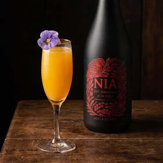 Copa flauta con jugo de naranja y una flor morada, junto a la botella de Nía Açaí & Flores