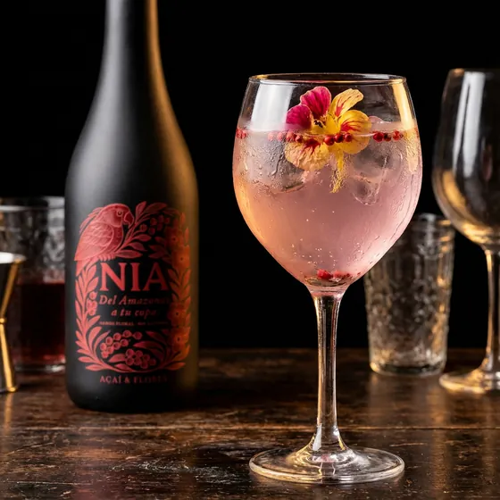 Copa balón rosada con una flor comestible, junto a la botella de Nía Açaí & Flores